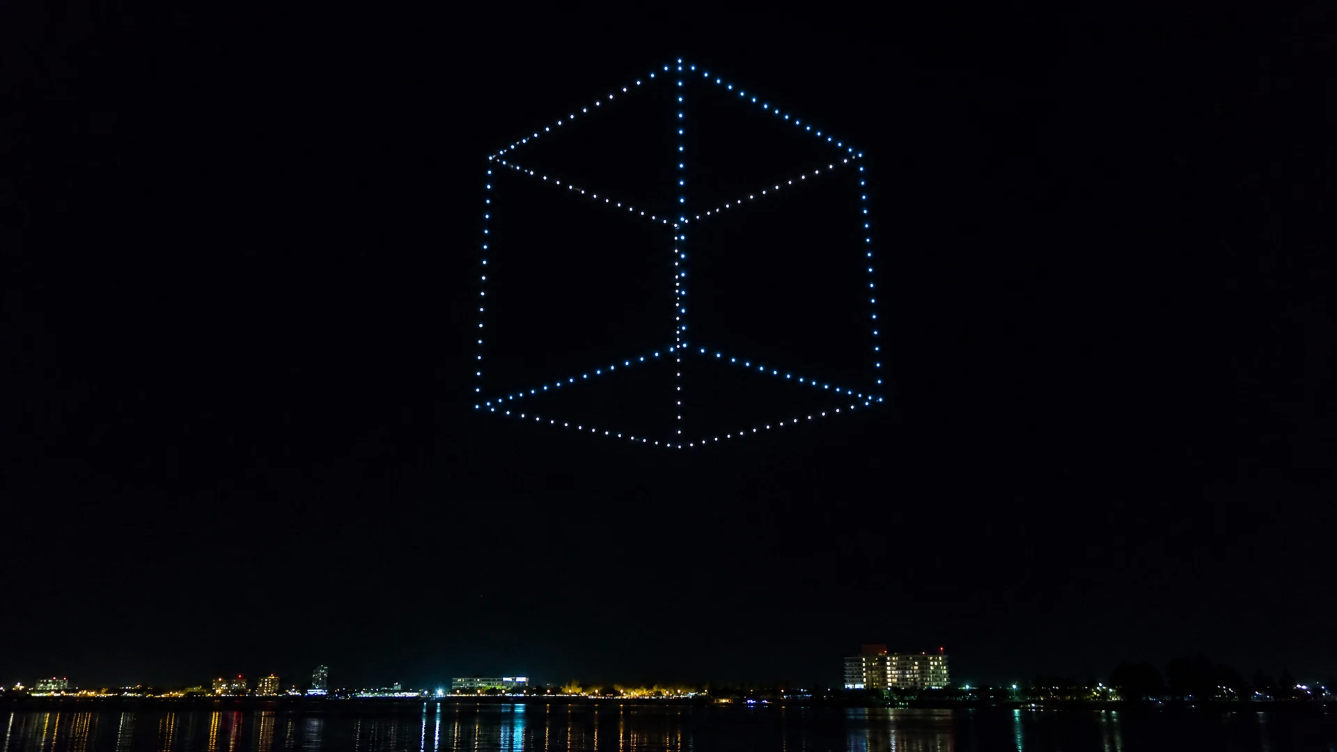 Three-dimensional cube outlined in drone lights above the sea
